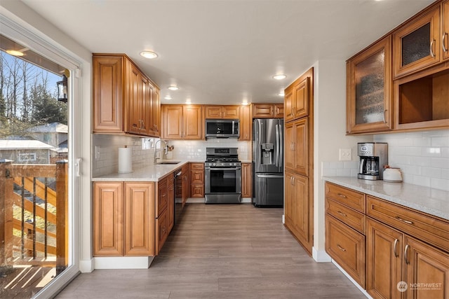 kitchen with appliances with stainless steel finishes, tasteful backsplash, sink, light stone counters, and light hardwood / wood-style floors