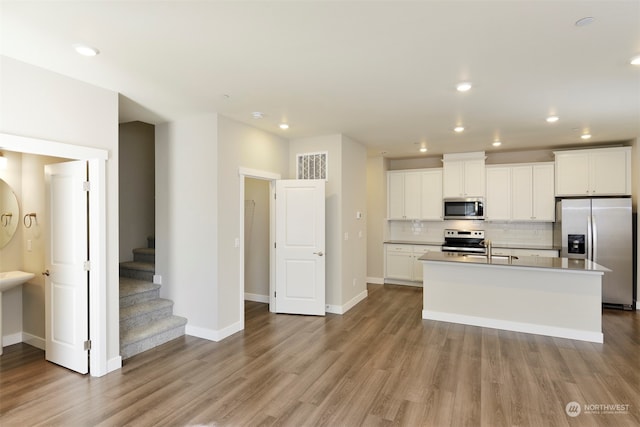 kitchen featuring stainless steel appliances, an island with sink, tasteful backsplash, and white cabinets