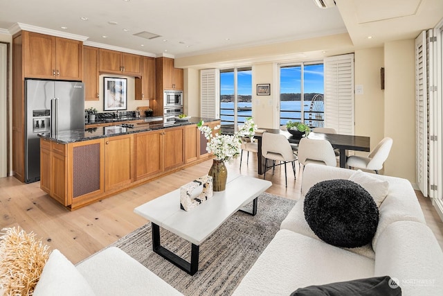 kitchen featuring a water view, dark stone countertops, light wood-type flooring, ornamental molding, and stainless steel appliances