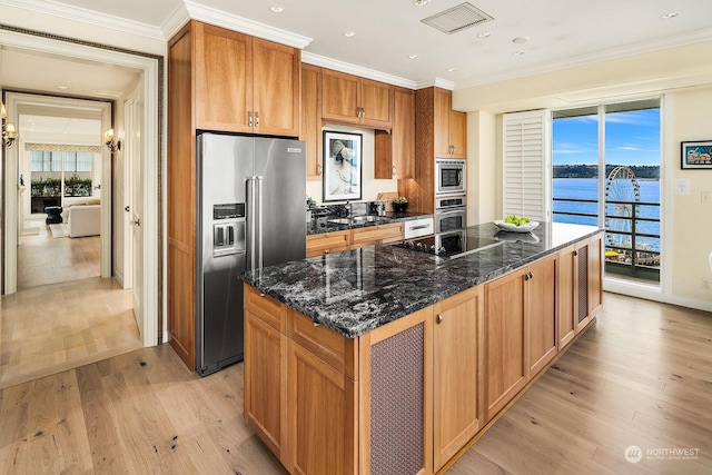 kitchen with a water view, dark stone countertops, ornamental molding, appliances with stainless steel finishes, and a kitchen island