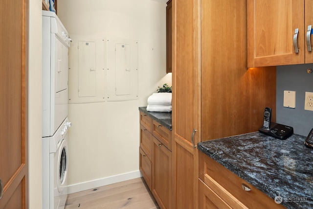 clothes washing area featuring stacked washer / drying machine, light hardwood / wood-style flooring, and cabinets