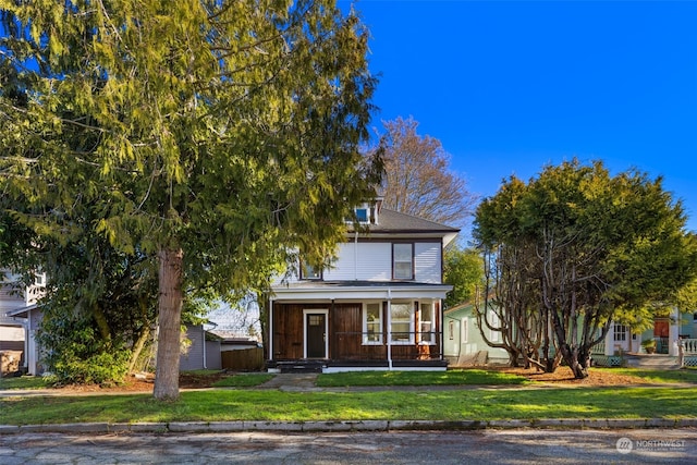 view of property hidden behind natural elements with a porch and a front yard