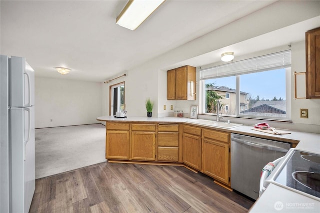 kitchen with a peninsula, a sink, light countertops, stainless steel dishwasher, and freestanding refrigerator