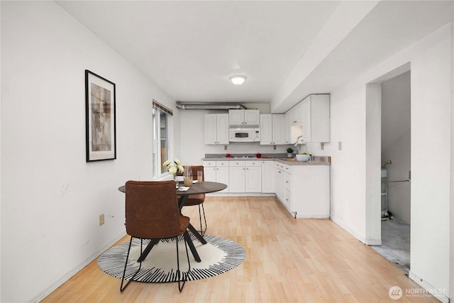 kitchen with white microwave, light wood-style flooring, baseboards, white cabinets, and light countertops