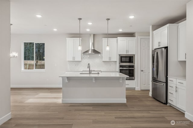 kitchen featuring hanging light fixtures, appliances with stainless steel finishes, wall chimney range hood, and white cabinets