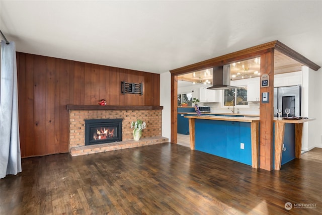 kitchen featuring a fireplace, island range hood, dark wood-type flooring, and stainless steel refrigerator