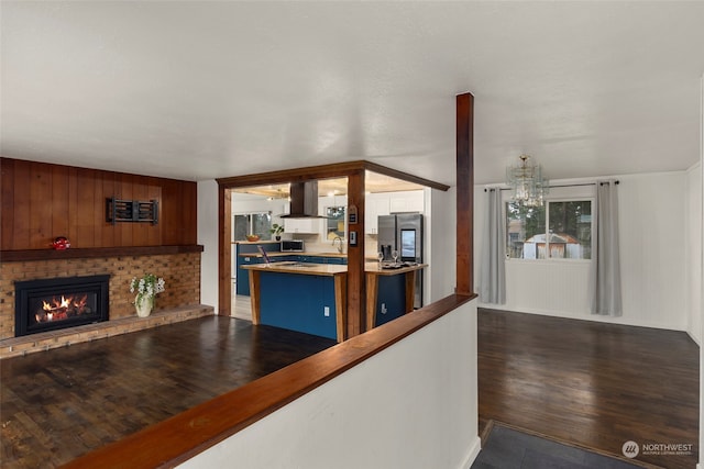 kitchen with an inviting chandelier, dark hardwood / wood-style floors, stainless steel refrigerator with ice dispenser, island exhaust hood, and a brick fireplace