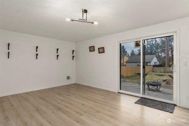 unfurnished room featuring an inviting chandelier and light hardwood / wood-style flooring