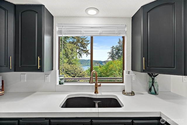 kitchen featuring a sink, a textured ceiling, dark cabinetry, and light countertops