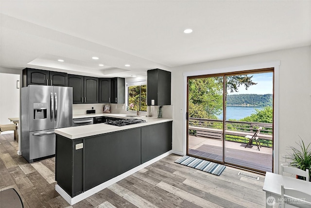 kitchen with light wood-style floors, appliances with stainless steel finishes, a peninsula, and light countertops