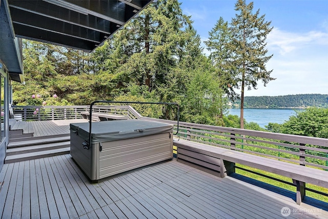 deck with a forest view, a water view, and a hot tub