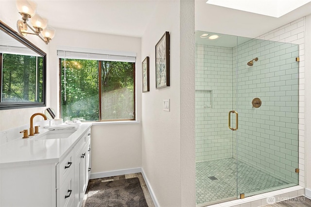 bathroom with baseboards, vanity, a healthy amount of sunlight, and a shower stall