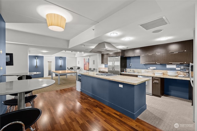 kitchen featuring dark wood-type flooring, dark brown cabinetry, appliances with stainless steel finishes, a kitchen island, and island exhaust hood