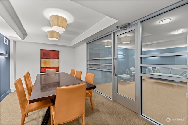 dining space with light colored carpet and a raised ceiling