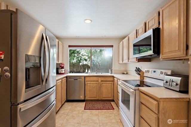 kitchen with appliances with stainless steel finishes, sink, light tile patterned floors, and light brown cabinetry