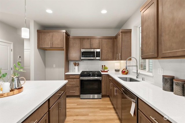 kitchen featuring appliances with stainless steel finishes, decorative light fixtures, sink, decorative backsplash, and light wood-type flooring