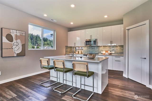 kitchen with white cabinetry, sink, a kitchen island with sink, and a breakfast bar area