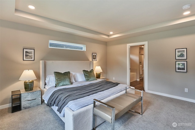 carpeted bedroom featuring ensuite bathroom and a raised ceiling