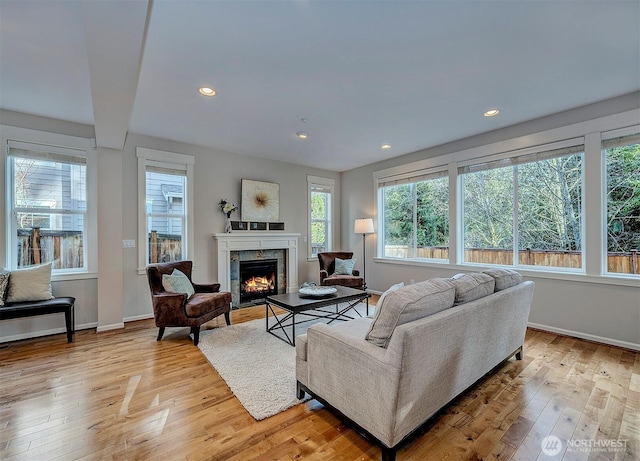 living area with a premium fireplace, recessed lighting, light wood-style flooring, and baseboards