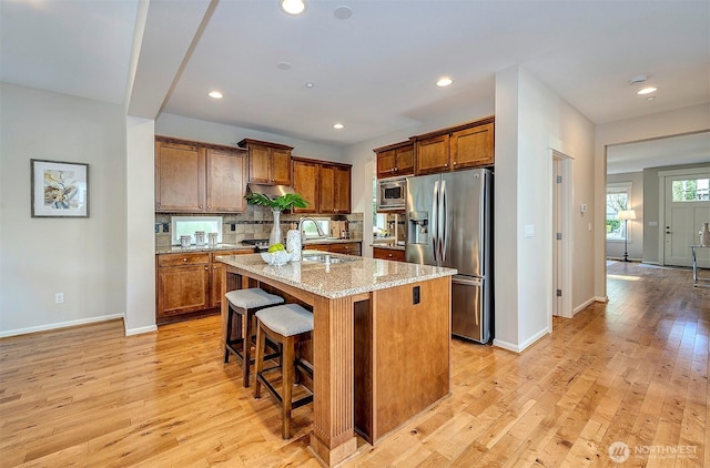 kitchen with stainless steel appliances, brown cabinets, a center island with sink, and light stone counters