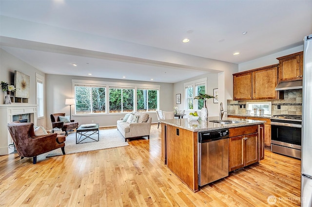 kitchen featuring a center island with sink, open floor plan, light stone countertops, stainless steel appliances, and a sink