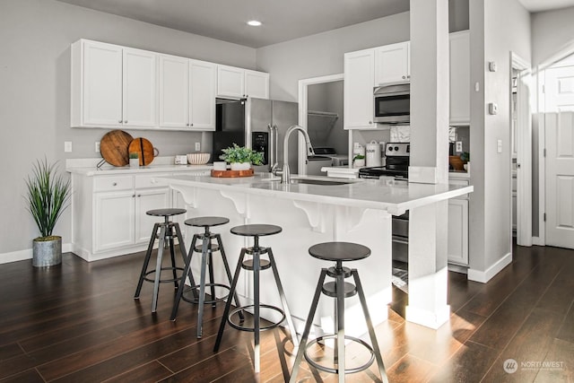 kitchen with sink, appliances with stainless steel finishes, an island with sink, white cabinets, and a kitchen bar