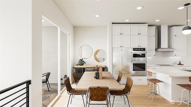 kitchen with pendant lighting, white cabinetry, double oven, light hardwood / wood-style floors, and wall chimney exhaust hood