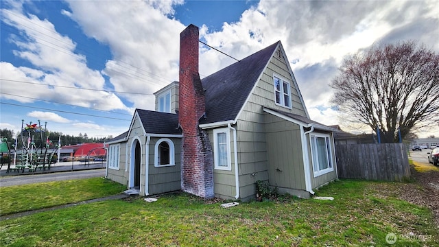 view of property exterior with roof with shingles, fence, a chimney, and a lawn