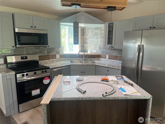 kitchen featuring a center island, light stone counters, a sink, decorative light fixtures, and stainless steel appliances