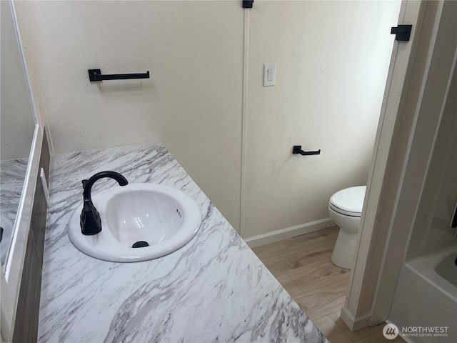 bathroom featuring a sink, baseboards, toilet, and a bathtub