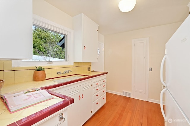 kitchen with white cabinetry, tile counters, sink, and white fridge