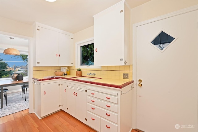 kitchen featuring sink, tasteful backsplash, pendant lighting, light hardwood / wood-style floors, and white cabinets