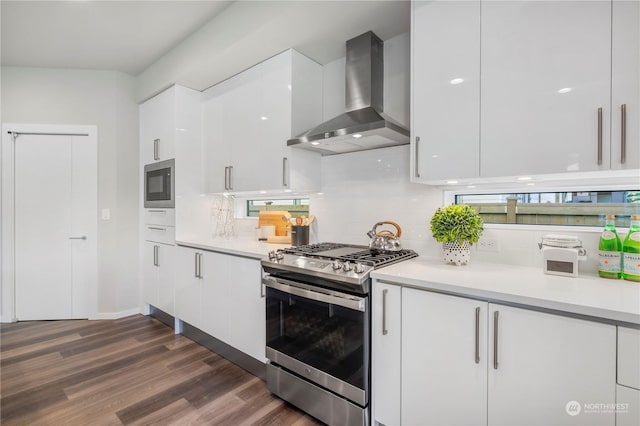 kitchen featuring appliances with stainless steel finishes, white cabinetry, dark hardwood / wood-style floors, tasteful backsplash, and wall chimney exhaust hood