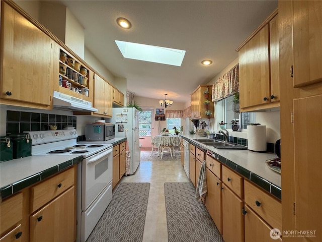 kitchen with a skylight, backsplash, a sink, white appliances, and under cabinet range hood