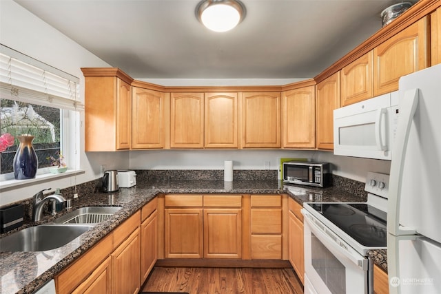 kitchen with sink, white appliances, light hardwood / wood-style floors, and dark stone counters