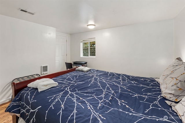 bedroom with heating unit and wood-type flooring