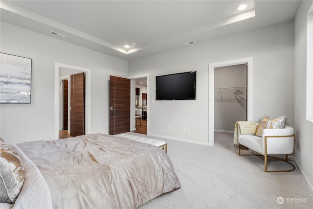 bedroom with light carpet, a closet, a spacious closet, and a raised ceiling