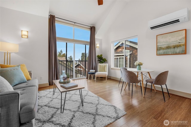 living room featuring a towering ceiling, baseboards, wood finished floors, and a wall mounted air conditioner