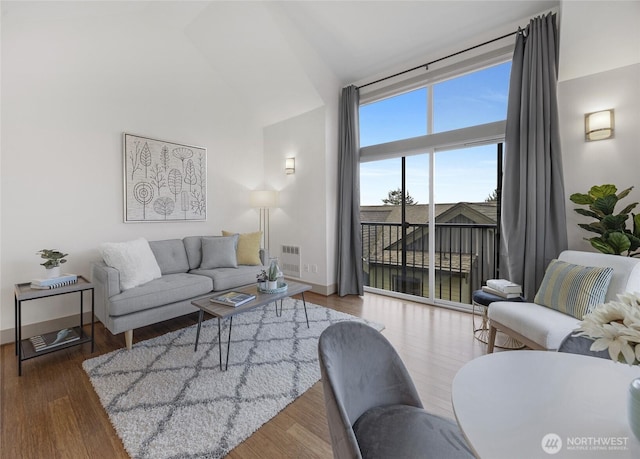 living area featuring visible vents, a towering ceiling, baseboards, and wood finished floors