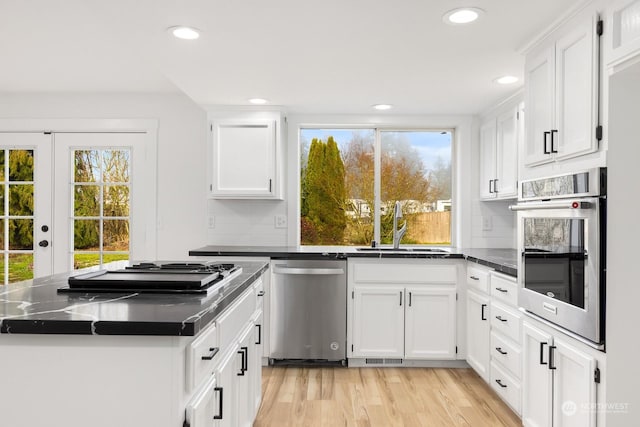 kitchen with sink, white cabinets, stainless steel appliances, light hardwood / wood-style floors, and backsplash