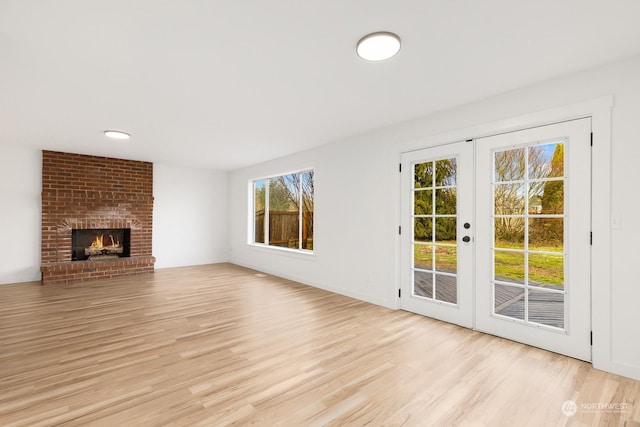 unfurnished living room featuring french doors, a brick fireplace, and light hardwood / wood-style flooring