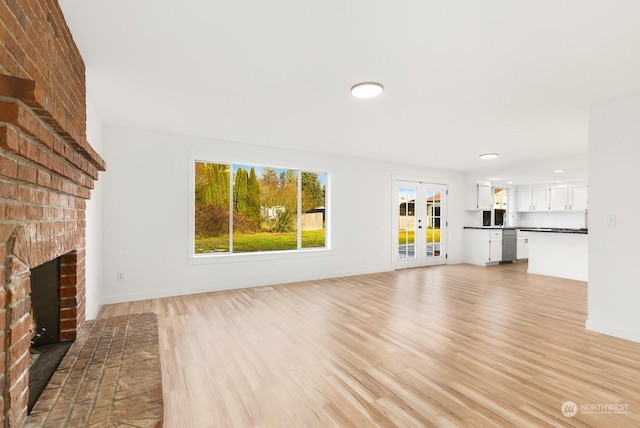 unfurnished living room featuring french doors, a fireplace, and light hardwood / wood-style flooring