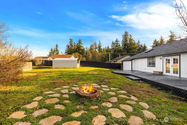 view of yard with a shed, a wooden deck, a fire pit, and french doors