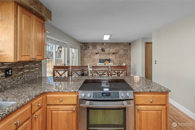 kitchen featuring backsplash, electric range, light hardwood / wood-style floors, and dark stone counters