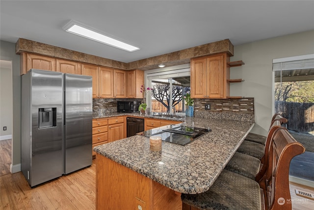 kitchen featuring dark stone countertops, a breakfast bar, kitchen peninsula, and black appliances