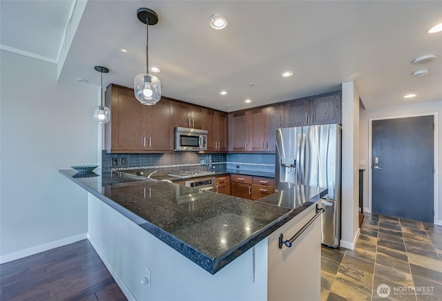 kitchen featuring kitchen peninsula, stainless steel appliances, dark stone counters, decorative backsplash, and pendant lighting