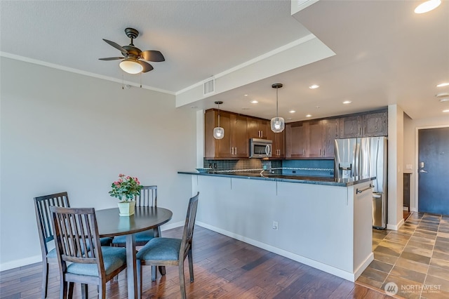 kitchen with appliances with stainless steel finishes, backsplash, pendant lighting, kitchen peninsula, and ornamental molding