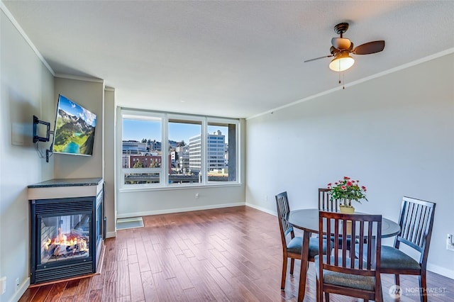 dining room featuring wood-type flooring, a multi sided fireplace, a textured ceiling, ceiling fan, and ornamental molding