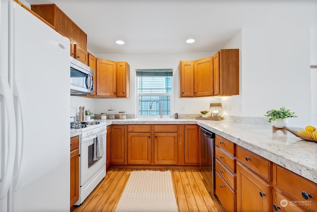 kitchen featuring light stone counters, white appliances, light hardwood / wood-style floors, and sink