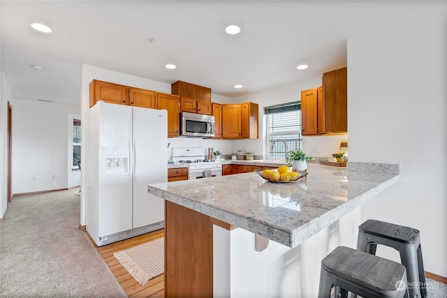 kitchen with sink, light wood-type flooring, a kitchen breakfast bar, kitchen peninsula, and white appliances